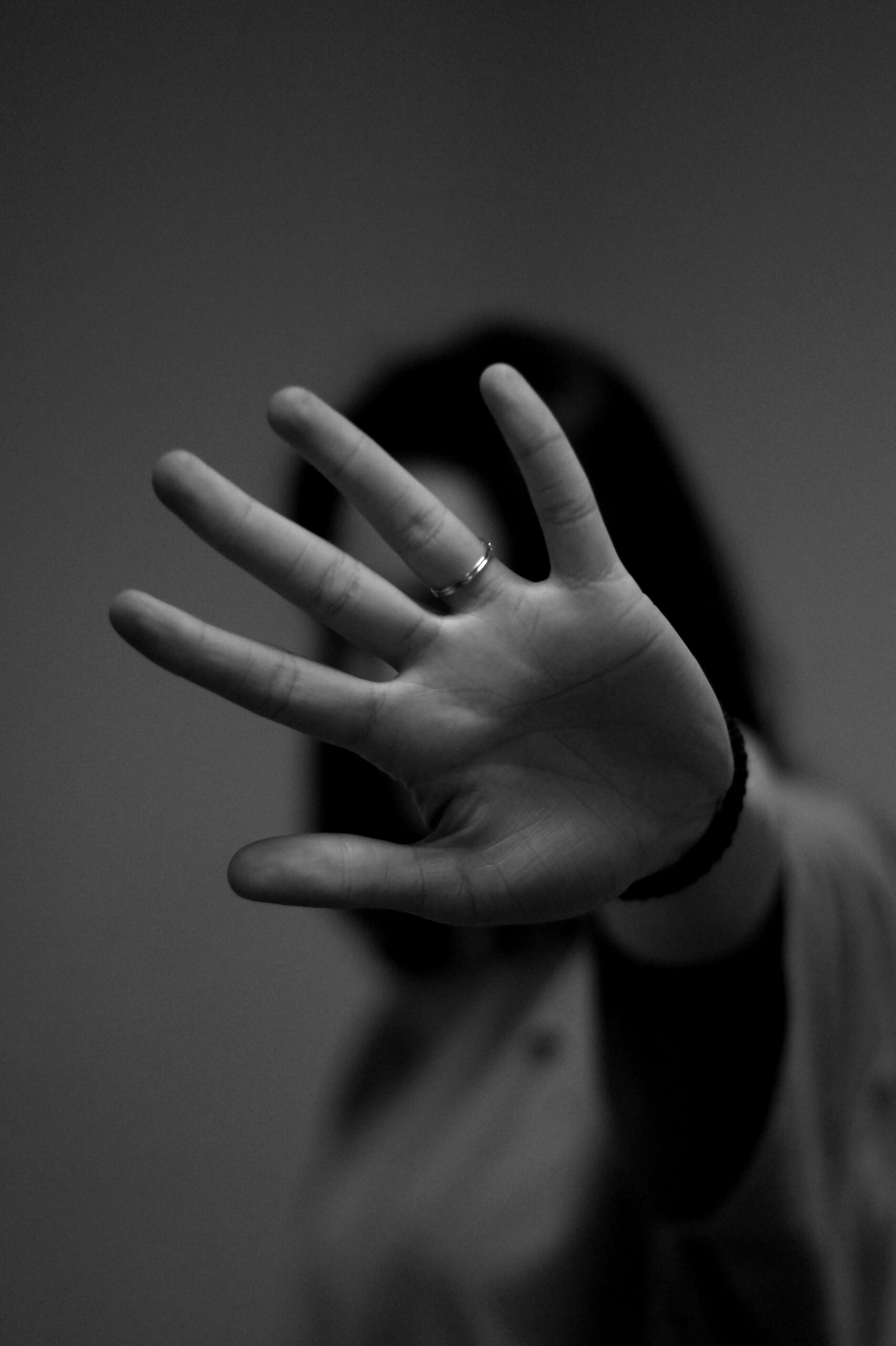 A woman with her hand in front of her blocking her face. Grey-scaled. Photo by Mattia Ascenzo on Unsplash.